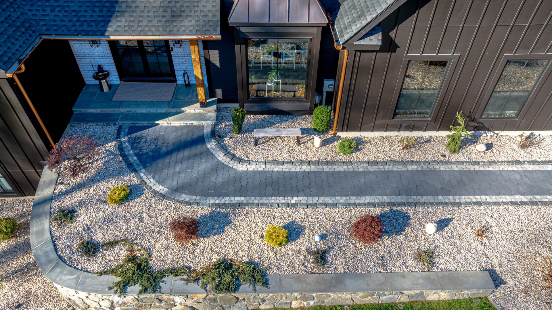 Aerial view showcasing a beautifully designed front walkway made from stylish hexagonal stone pavers, bordered by decorative cobblestone, and complemented by neatly landscaped gravel gardens and shrubs, leading elegantly to a modern home's entrance.
